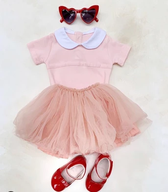 pink baby outfit flay lay on the floor with red shoes and sunglasses