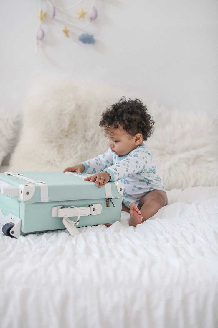 baby sitting on bed playing with mint suitcase