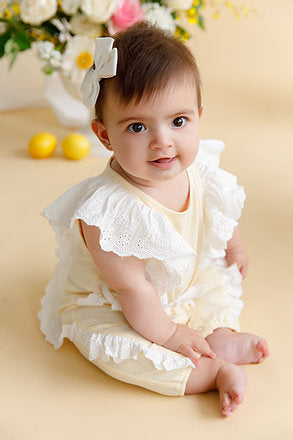 baby girl sitting on ground in white and  lemon jumpsuit